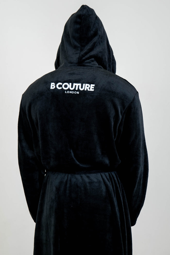 A person wears the Earnshaw Dressing Gown - Black with "B COUTURE LONDON" in white on the upper back. The background is plain and light-colored.