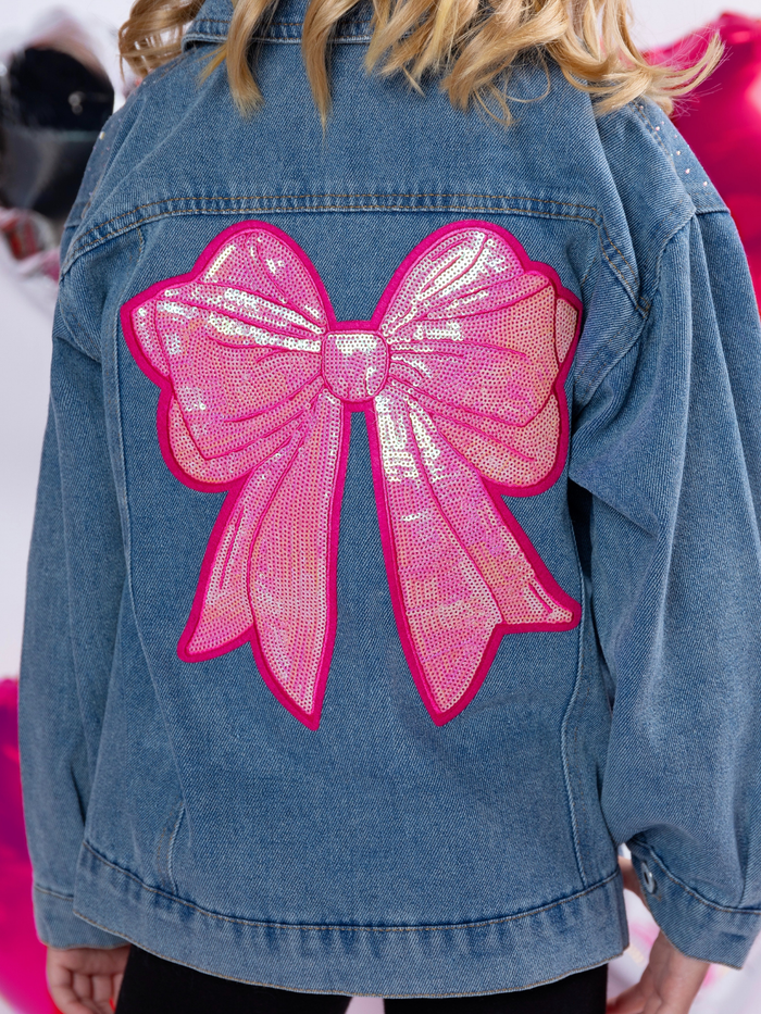 Girl wearing denim jacket with large pink sequin bow on the back