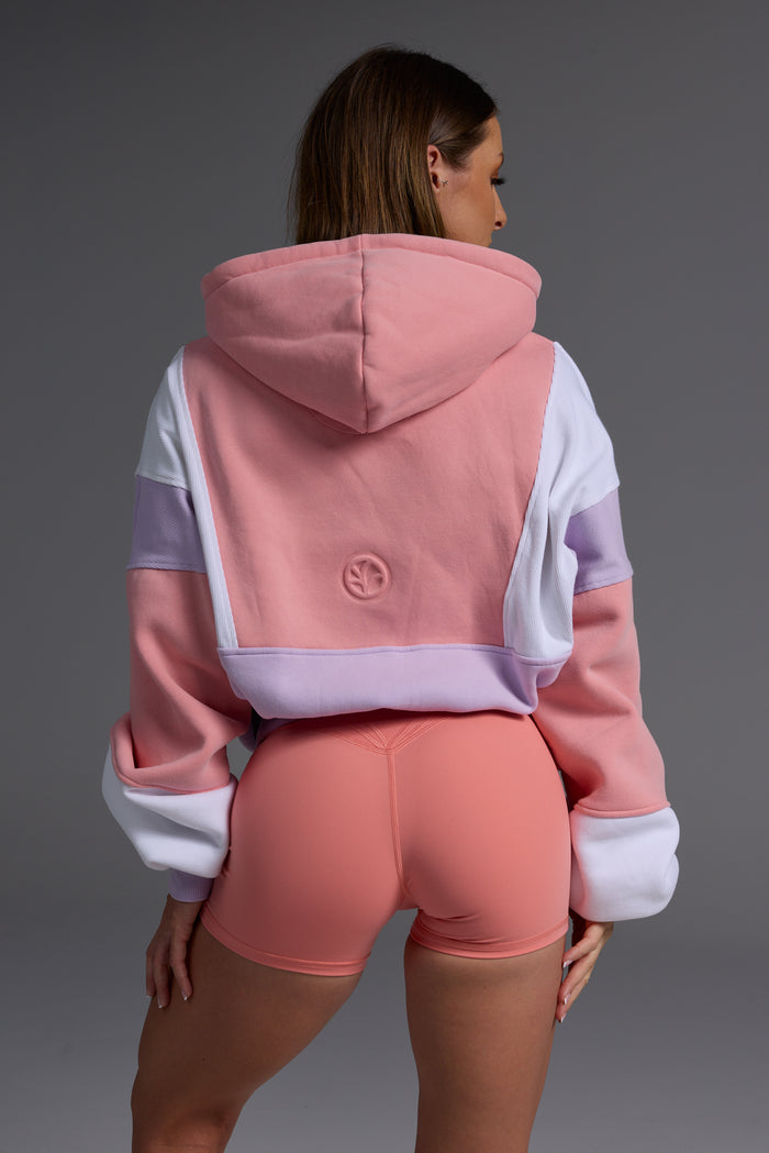 Back view of woman in peach, lilac and white oversized fleece hoodie with coral bike shorts showing relaxed fit