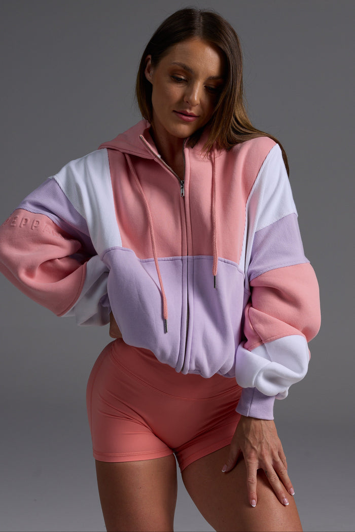 Woman in peach, lilac and white fleece hoodie with coral bike shorts in relaxed standing pose