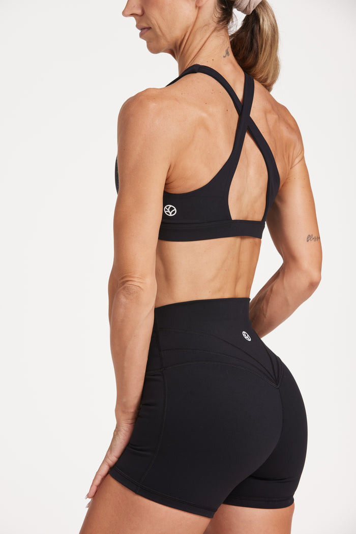 Buttery soft high waisted women's gym shorts with 4" inseam with curved stitched detailing for a butt shaping effect, and no front rise seam, paired with a high neck women's sports bra with a supportive elasticated hem and triple layered fabric with removable pads for extra support and crossover back straps in Black.