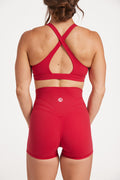 Buttery soft high waisted women's gym shorts with 4" inseam with curved stitched detailing for a butt shaping effect, and no front rise seam, paired with a high neck women's sports bra with a supportive elasticated hem and triple layered fabric with removable pads for extra support and crossover back straps in Raspberry red.
