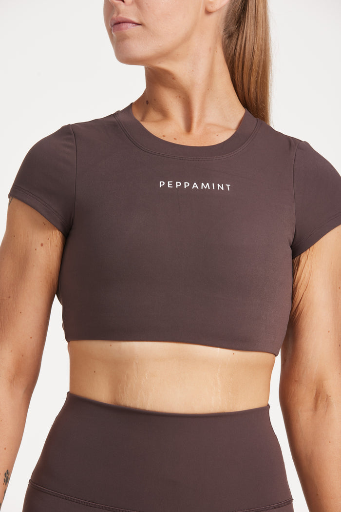 Buttery soft high waisted women's gym tights with curved hem stitched detailing for a butt shaping effect, and no front rise seam, paired with an open back women's crop t-shirt with a supportive elasticated hem and triple layered fabric with removable pads for extra support and aesthetic cross back straps in dark chocolate.