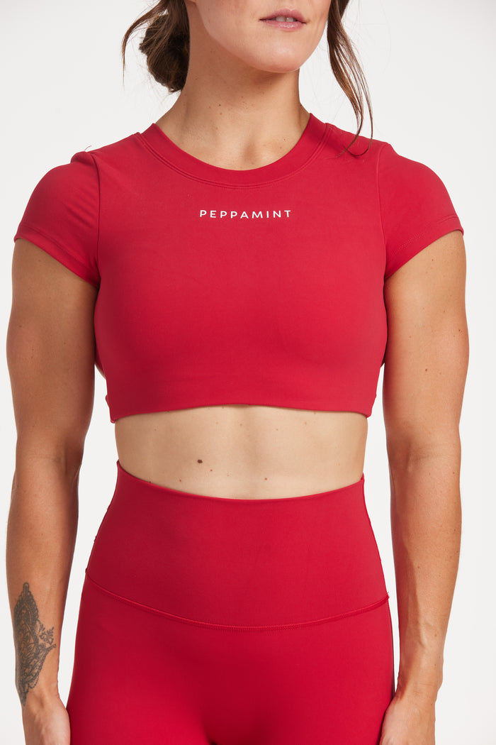 Buttery soft high waisted women's gym tights with curved hem stitched detailing for a butt shaping effect, and no front rise seam, paired with an open back women's crop t-shirt with a supportive elasticated hem and triple layered fabric with removable pads for extra support and aesthetic cross back straps in Raspberry red.
