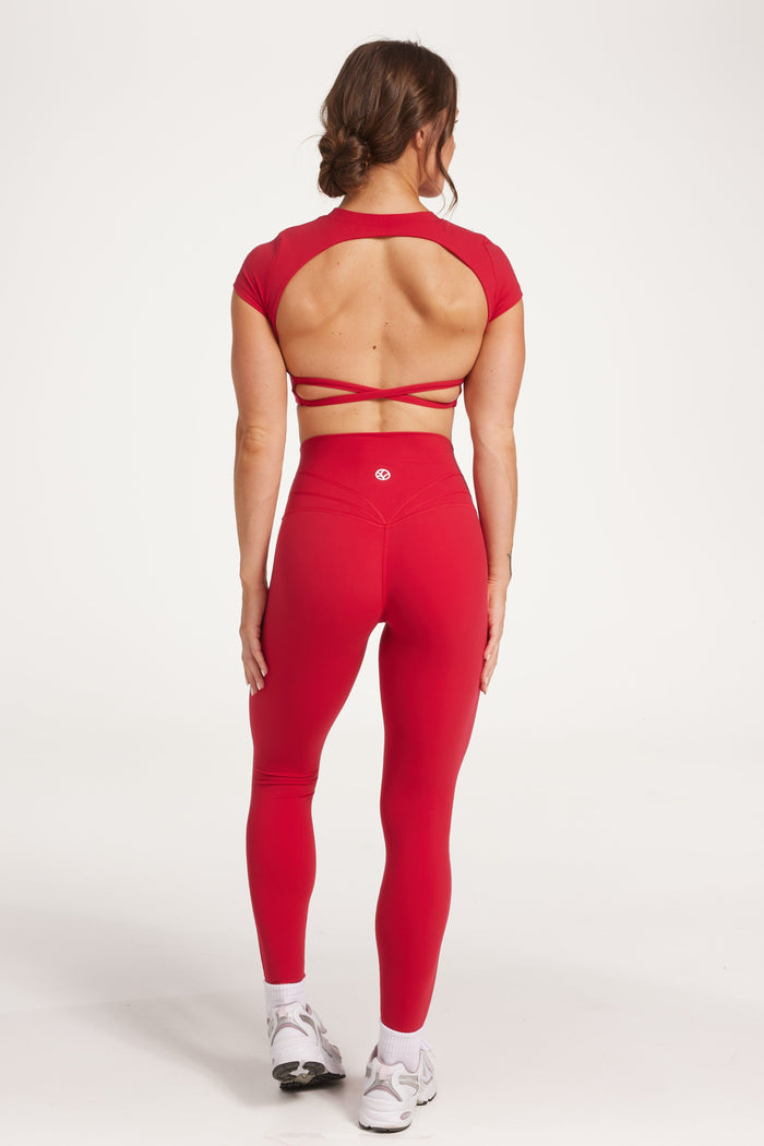 Buttery soft high waisted women's gym tights with curved hem stitched detailing for a butt shaping effect, and no front rise seam, paired with an open back women's crop t-shirt with a supportive elasticated hem and triple layered fabric with removable pads for extra support and aesthetic cross back straps in Raspberry red.