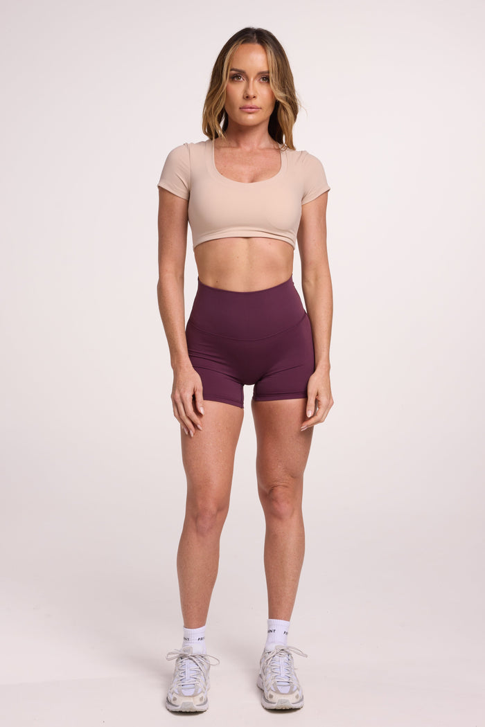 Buttery soft high waisted women's gym shorts with 4" inseam with curved stitched detailing for a butt shaping effect, and no front rise seam in plum purple paired with a V neck women's crop t-shirt with a supportive elasticated hem and triple layered fabric with removable pads for extra support in beige