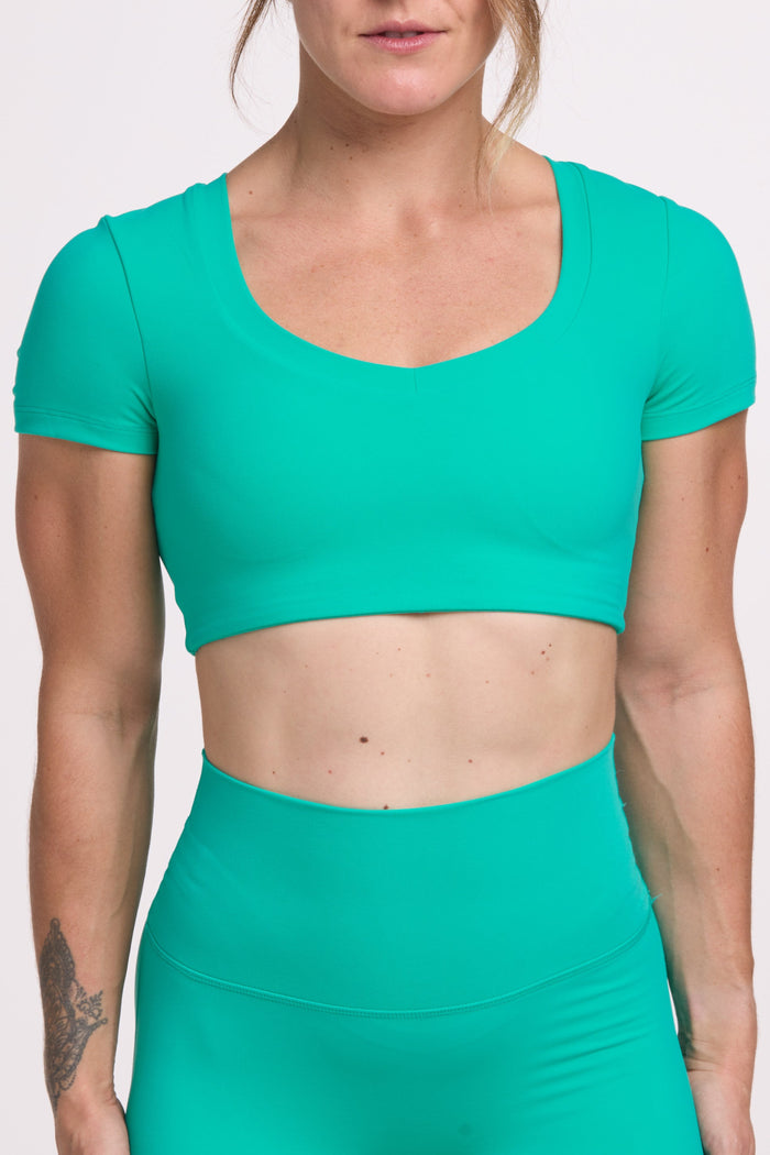 Buttery soft high waisted women's gym tights with curved back seam stitched detailing for a butt shaping effect, and no front rise seam paired with an V neck women's crop t-shirt with a supportive elasticated hem and triple layered fabric with removable pads for extra support in cyan green