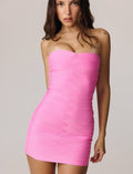 A woman with long brown hair models the TIGERMIST NIYA BANDAGE DRESS in pink—a strapless, sweetheart neckline mini dress—standing facing the camera against a plain light background, arms relaxed by her sides.