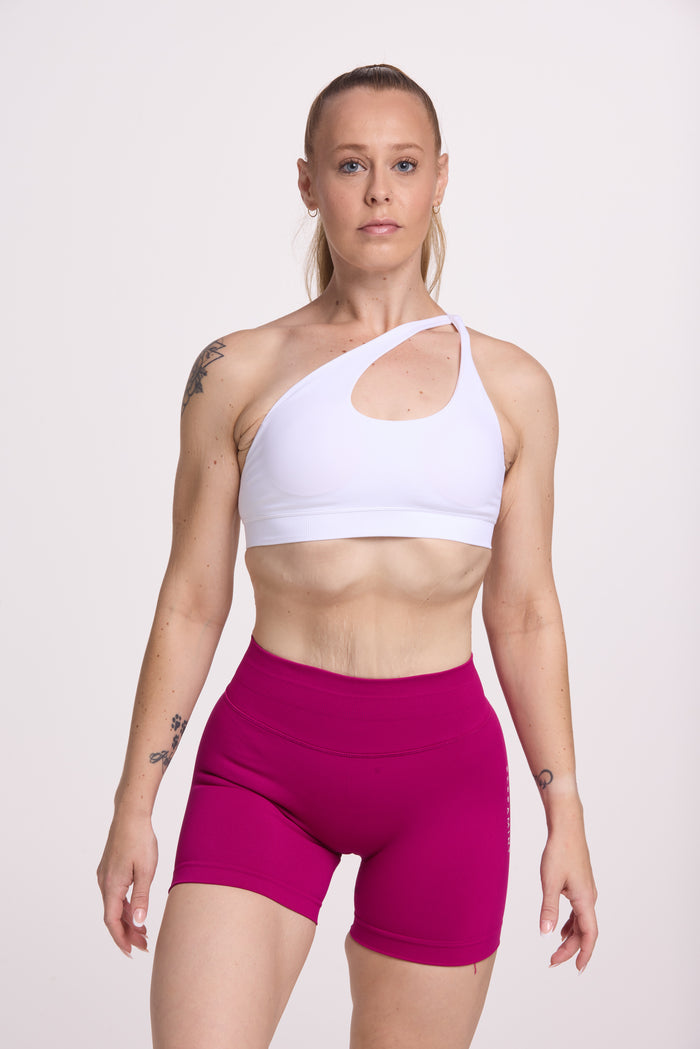 Front cross over strap activewear bra in seamless fabric with adjustable back straps, and ribbed supportive underbust band in white and seamless gym tights with booty contouring panels, invisible scrunch technology, sweetheart shaped back seams and thick supportive fabric in magenta pink