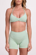 Minimalist bra with breast contouring panels and a ruched front seam to effortlessly shape the breasts, with a sleek back straps and halter neck design and seamless gym shorts with booty contouring panels, invisible scrunch technology, sweetheart shaped back seams and thick supportive fabric in mist green colour