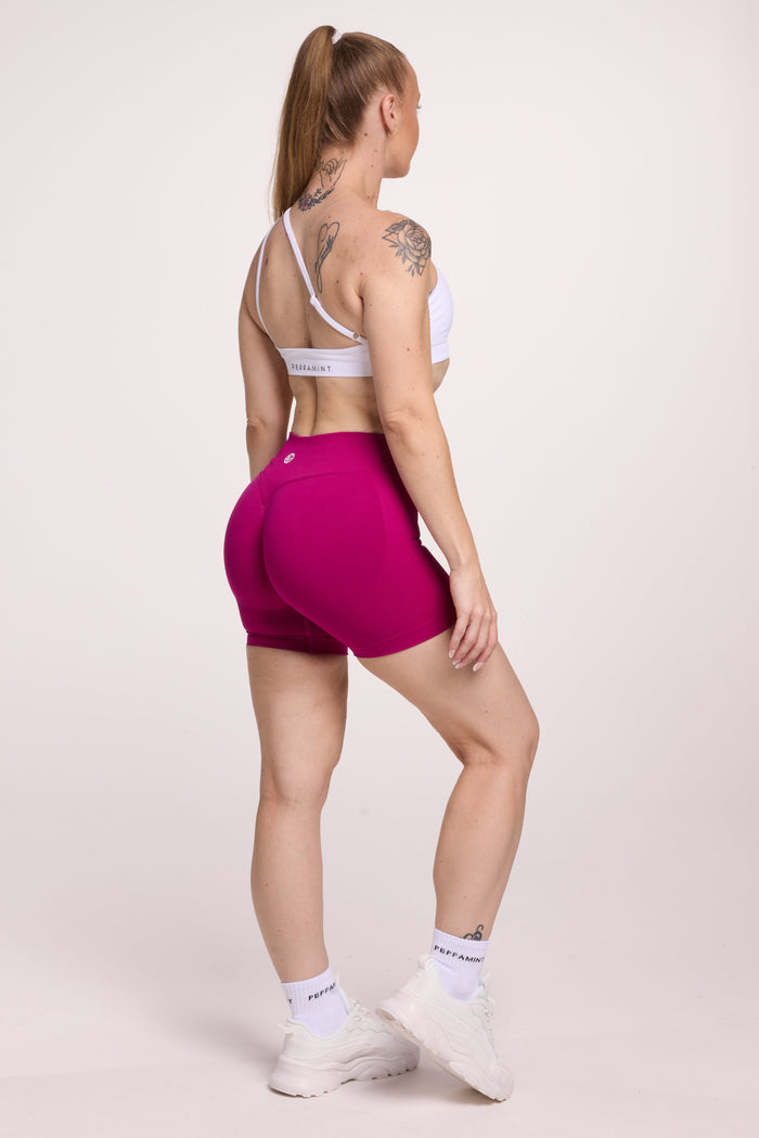 Front cross over strap activewear bra in seamless fabric with adjustable back straps, and ribbed supportive underbust band in white and seamless gym tights with booty contouring panels, invisible scrunch technology, sweetheart shaped back seams and thick supportive fabric in magenta pink