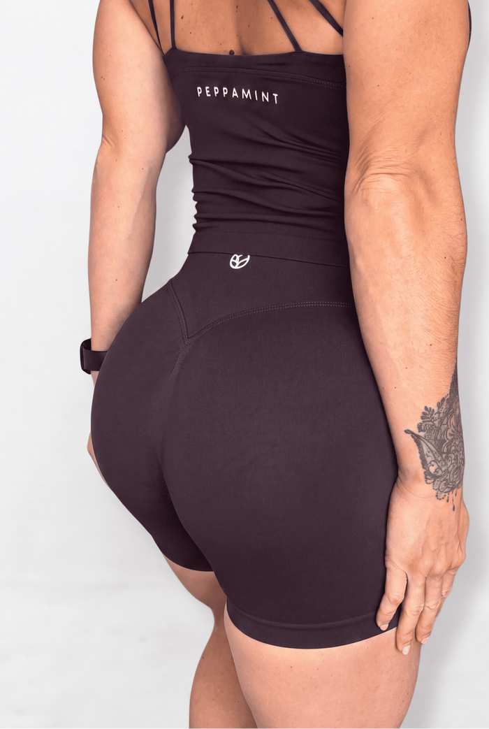 A woman shown from the back wearing a chocolate brown tank with thin strappy back details and matching fitted shorts. The tank has 'PEPPAMINT' printed in white near the upper back, and a small white logo on the waistband.