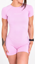 A woman modelling a light pink short-sleeve one-piece bodysuit against a plain white background.
