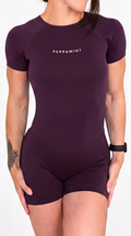 A woman modeling a chocolate plum short-sleeve bodysuit featuring the brand name 'PEPPAMINT' printed in white on the chest, set against a plain white background.
