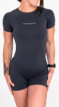 A woman modelling a dark grey short-sleeve one-piece bodysuit featuring the brand name 'PEPPAMINT' printed on the chest, set against a plain white background.