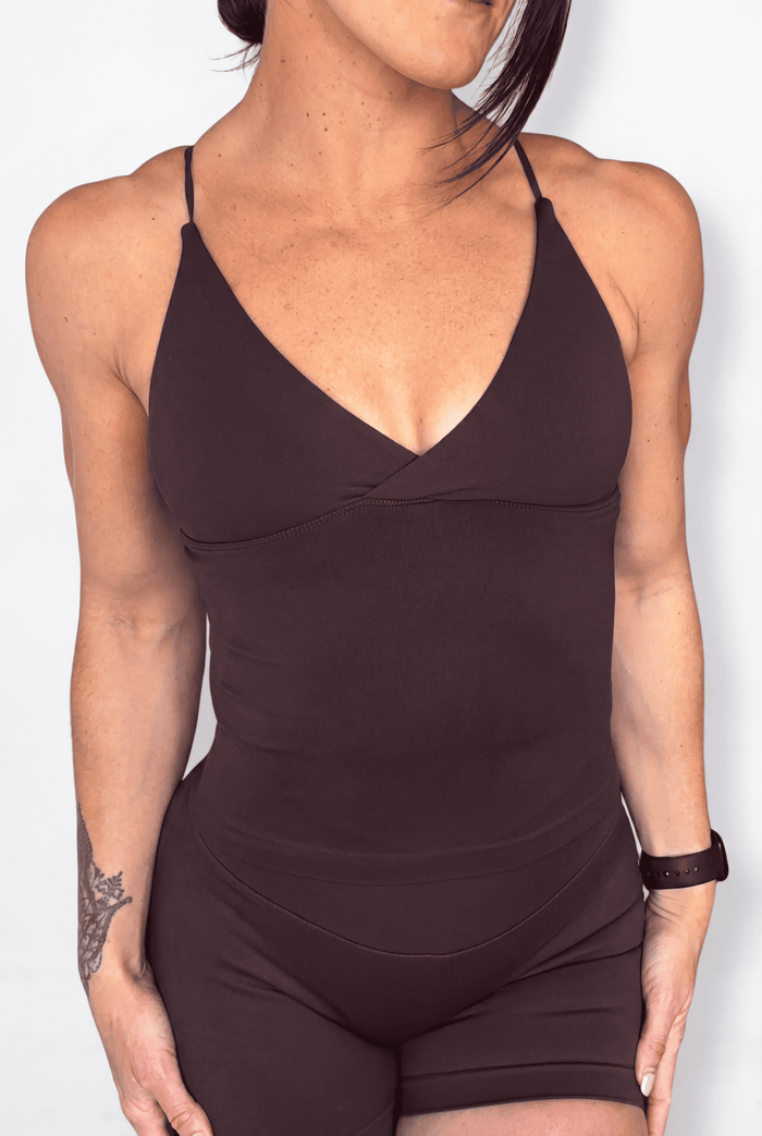 A woman wearing a dark brown athletic tank top with a V-neckline and matching shorts, shown against a plain light background.