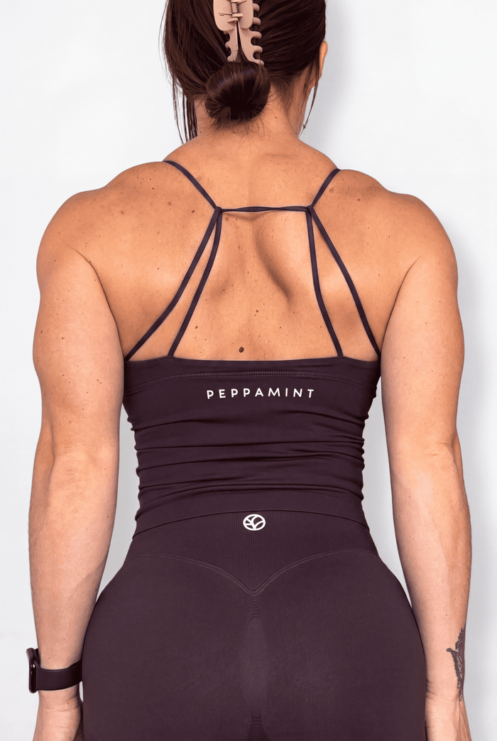 Rear view of a woman wearing a brown athletic tank with thin crisscross back straps and the brand name 'PEPPAMINT' printed on the upper back, set against a plain white background.