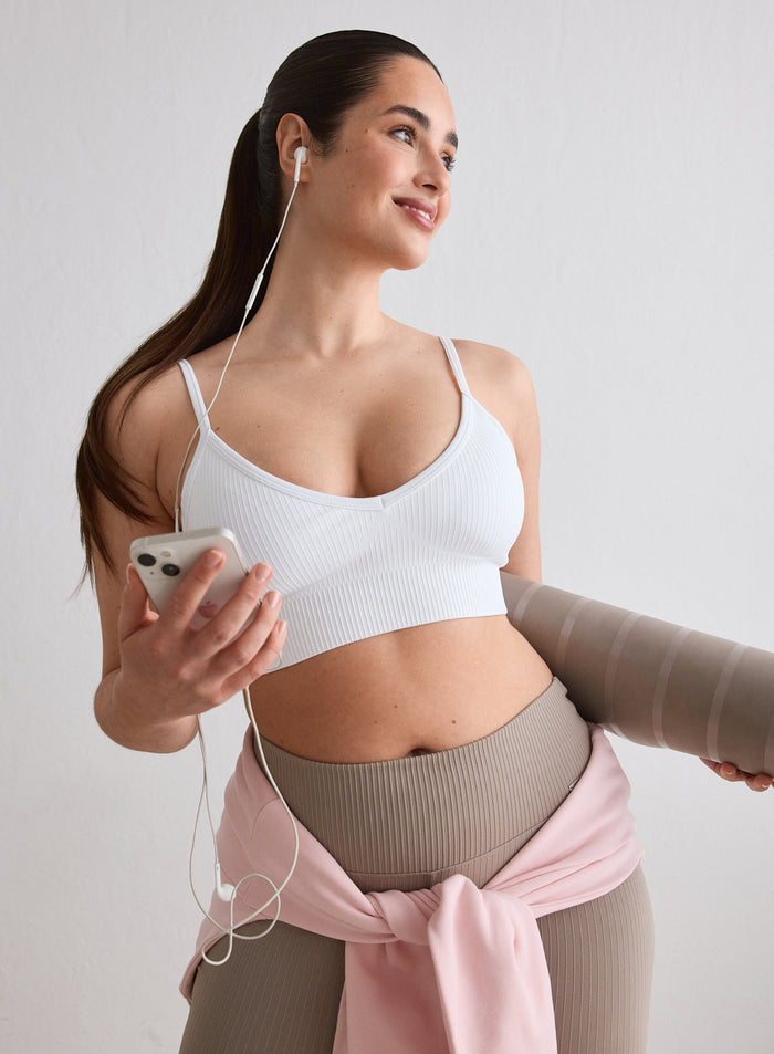 Nainen yllään aim'n White Ribbed Seamless Deep Cut Bra pitelemässä joogamattoa ja puhelinta [L-174cm]